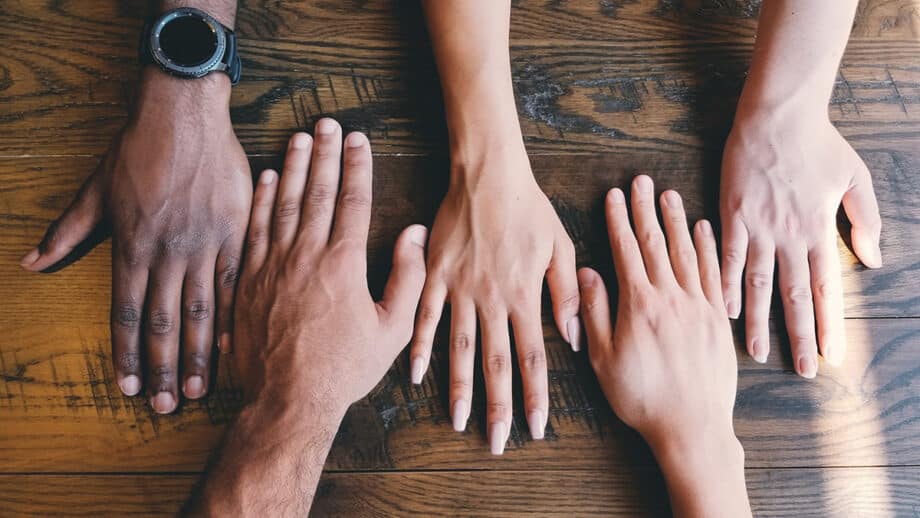 Four hands of different sizes and skin tones are placed side by side on a wooden surface.