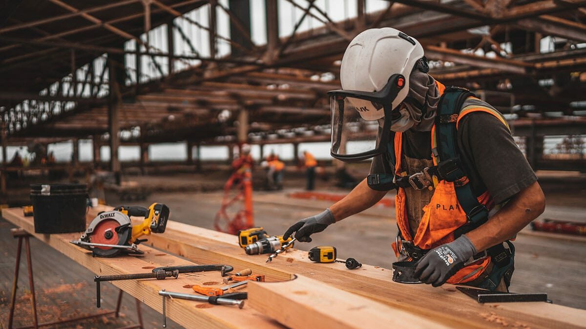 A construction worker is working on a wooden plank.