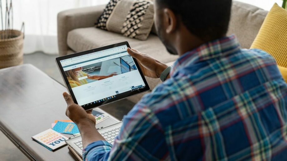 A man using a tablet in blue white and red plaid shirt.