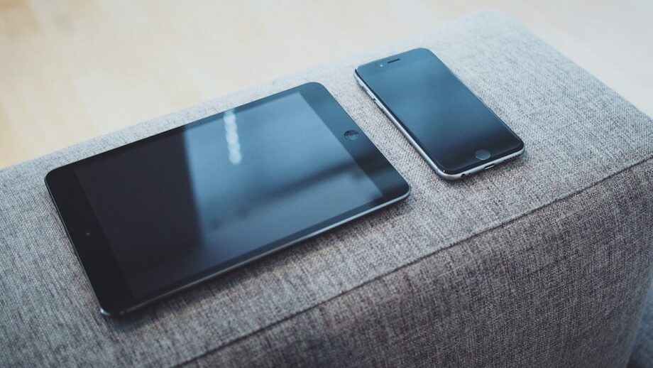 A gray couch with a tablet and phone on it.