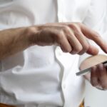 A person in a white shirt is using a smartphone with one hand, interacting with the screen via touch.