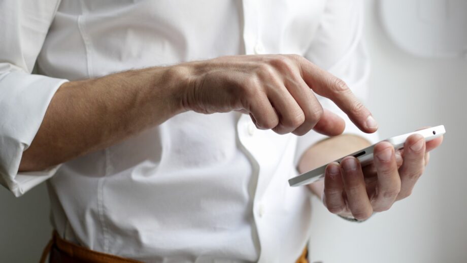 A person in a white shirt is using a smartphone with one hand, interacting with the screen via touch.