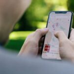 Person using a smartphone to navigate with a map app outdoors in a park setting.