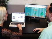 Two people sit at a desk, viewing a laptop and a monitor displaying a lead nurturing website.